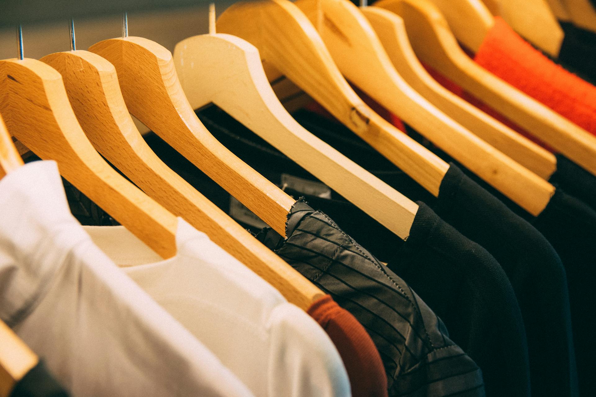 Clothes hang on wooden hangers in a row, showcasing assorted fabrics and colors, including white and black items.