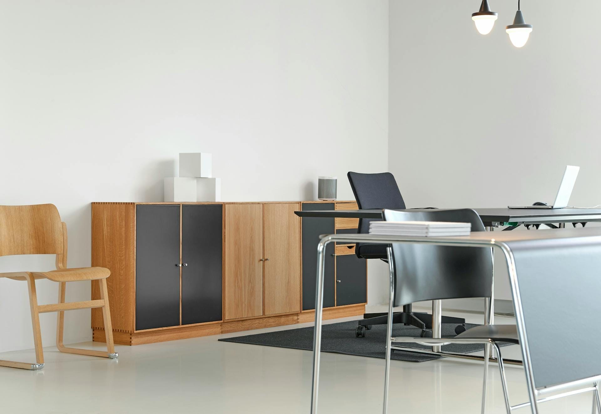 Modern office with wooden cabinets, chairs, desks, and a laptop on one desk; minimal decor and white walls.