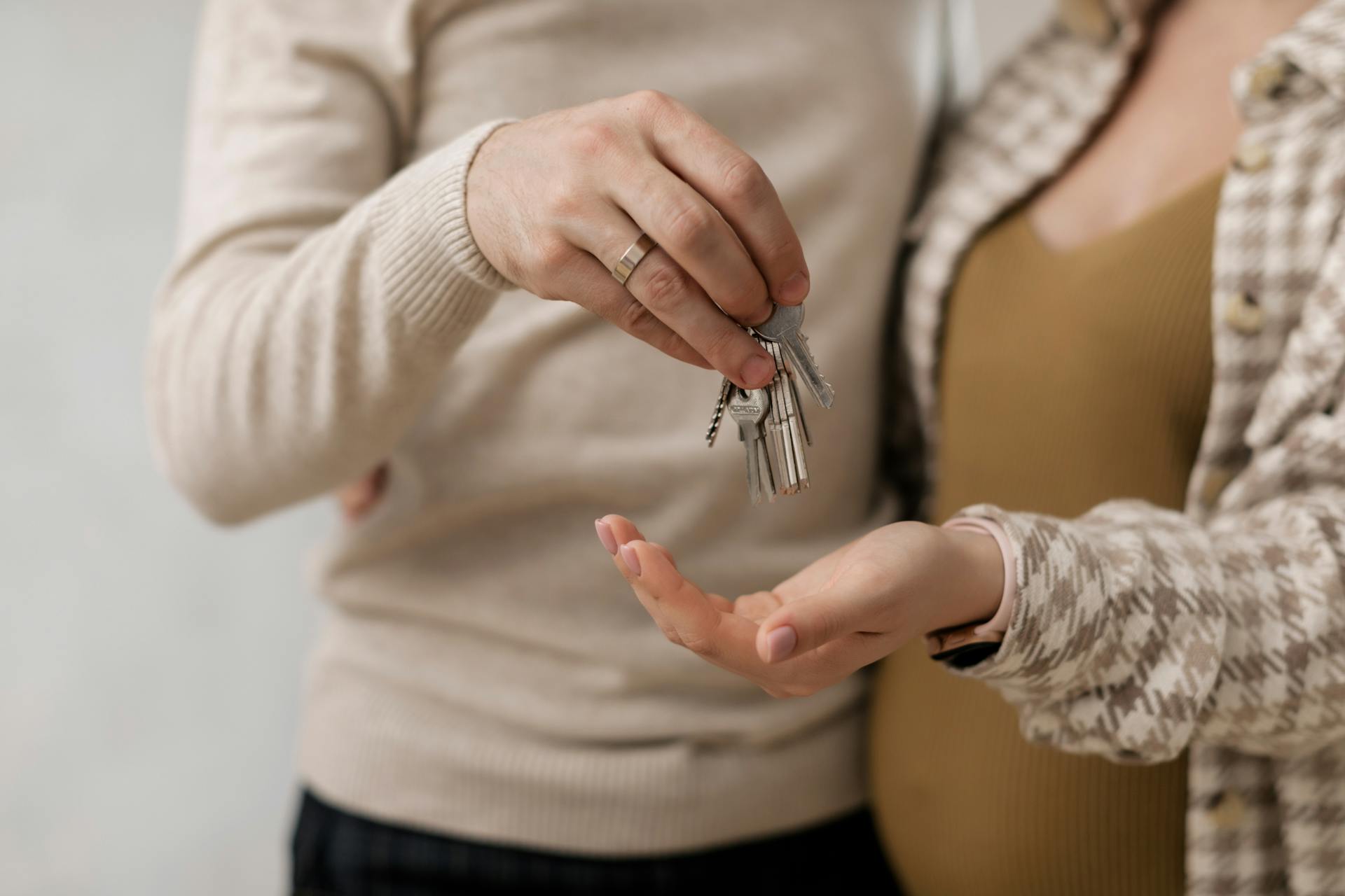 A person hands a set of keys to another person, implying a transfer or exchange, against a neutral background.