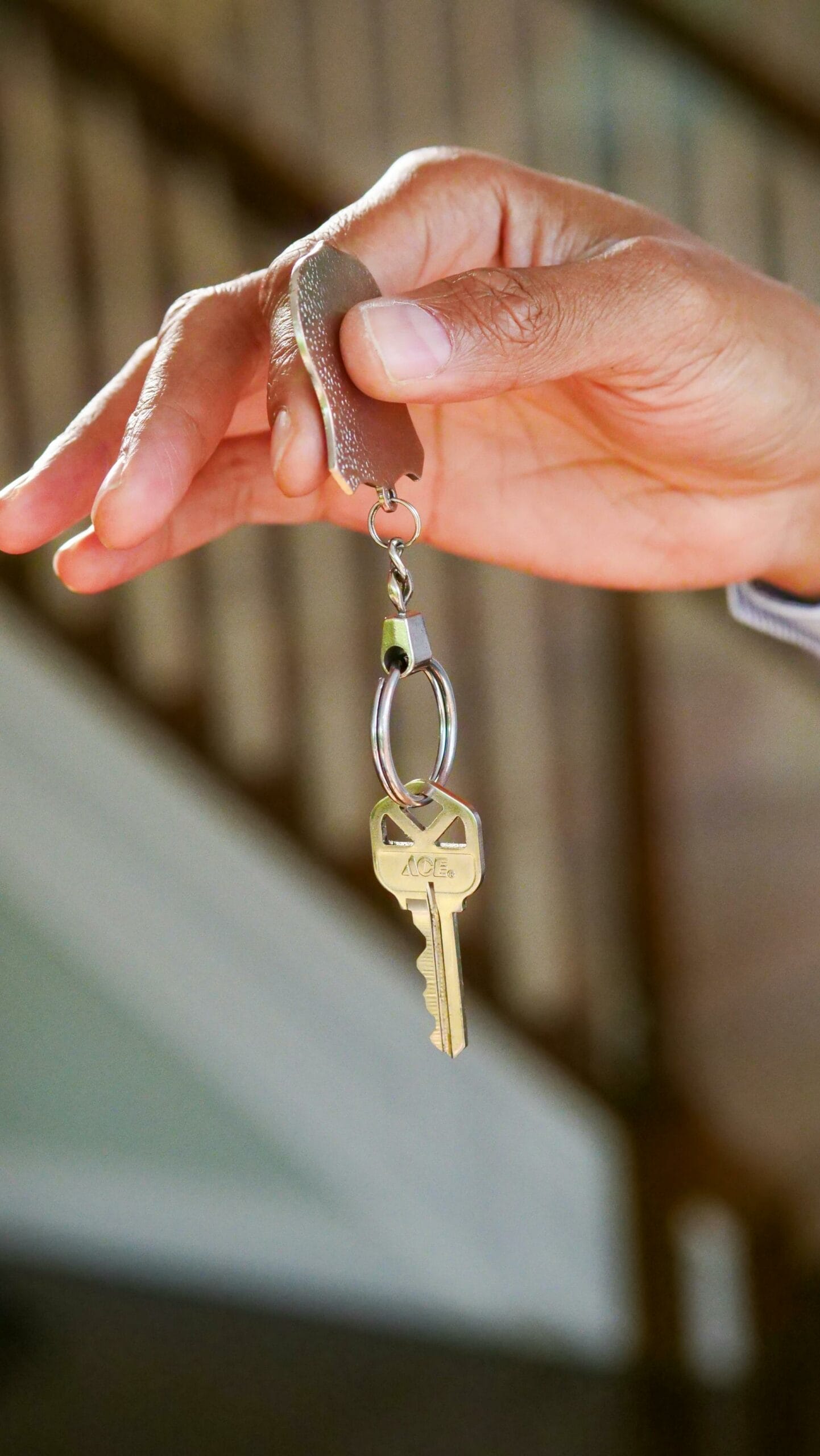 A hand holding a key with a square-shaped head, attached to a keyring with a small piece of leather.