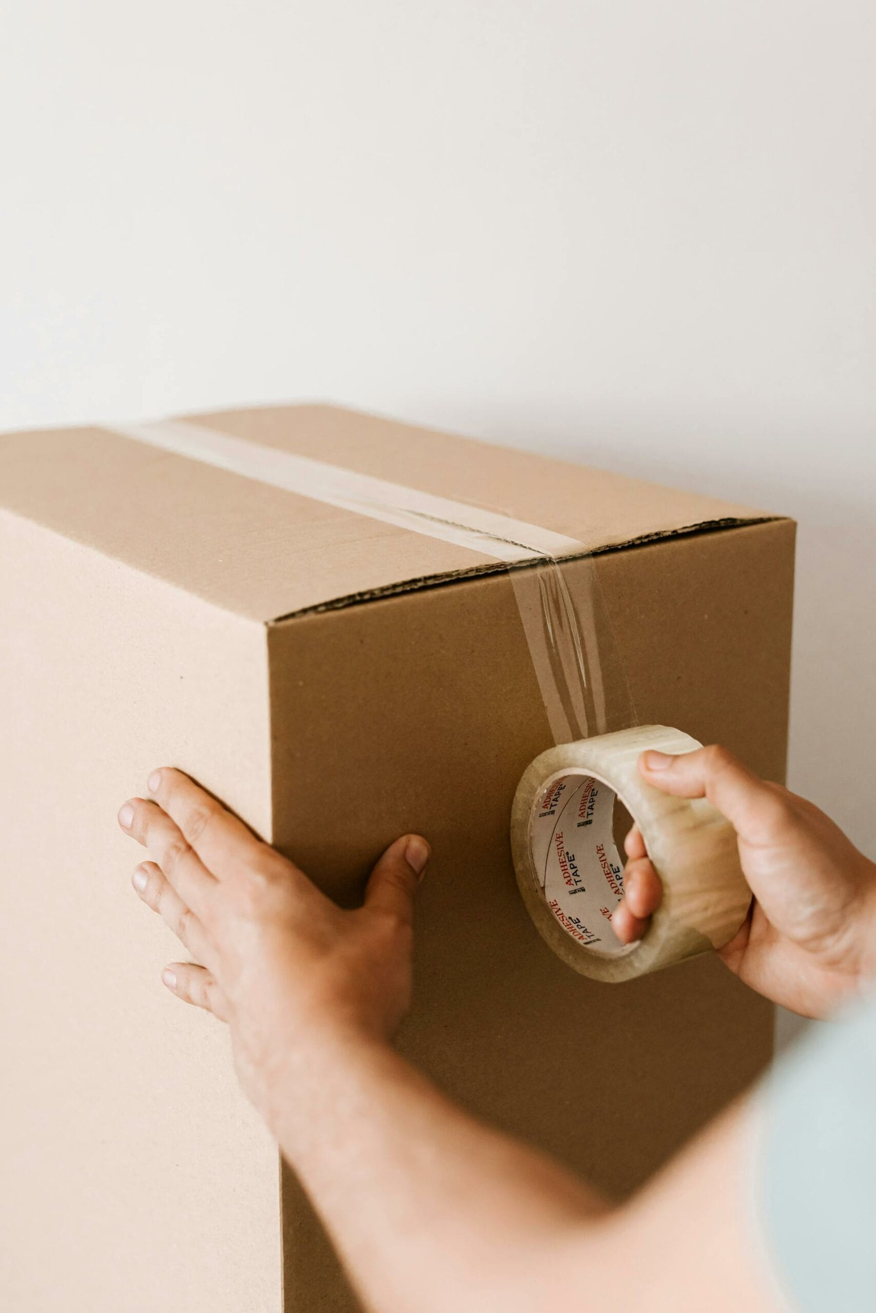 A person seals a cardboard box with clear packing tape.