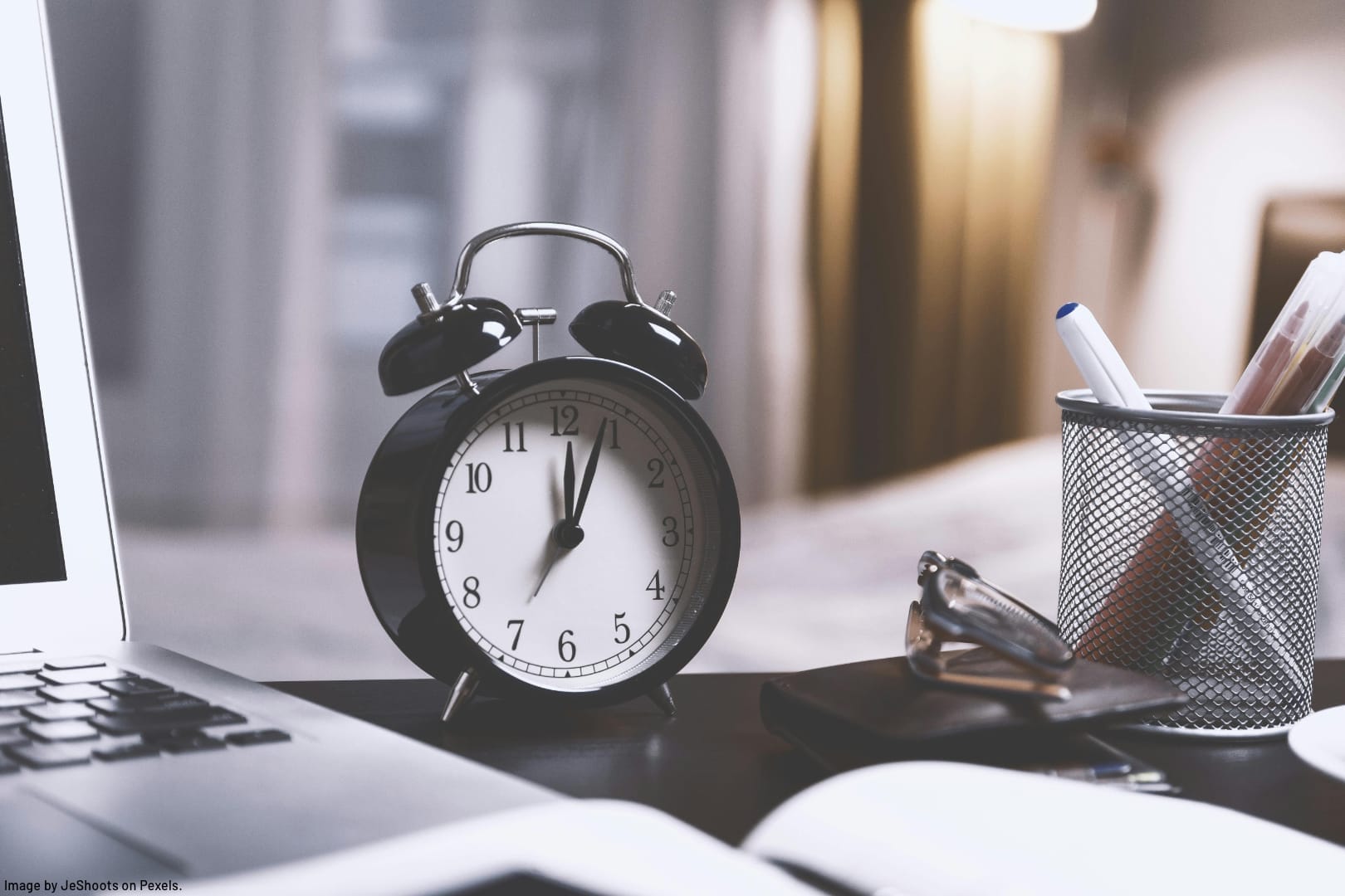 an alarm clock on a desk next to a computer and notebook representing how to give your productivity a big HIIT