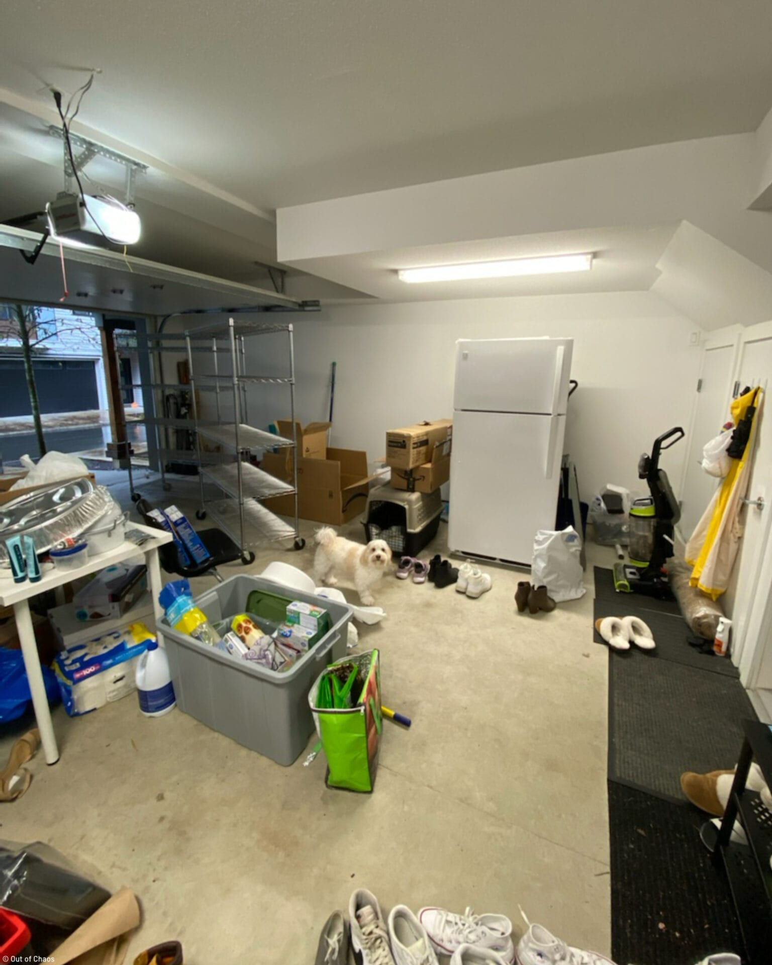 messy garage with boxes and cleaning supplies all over the floor and a fridge placed in the middle of the wall