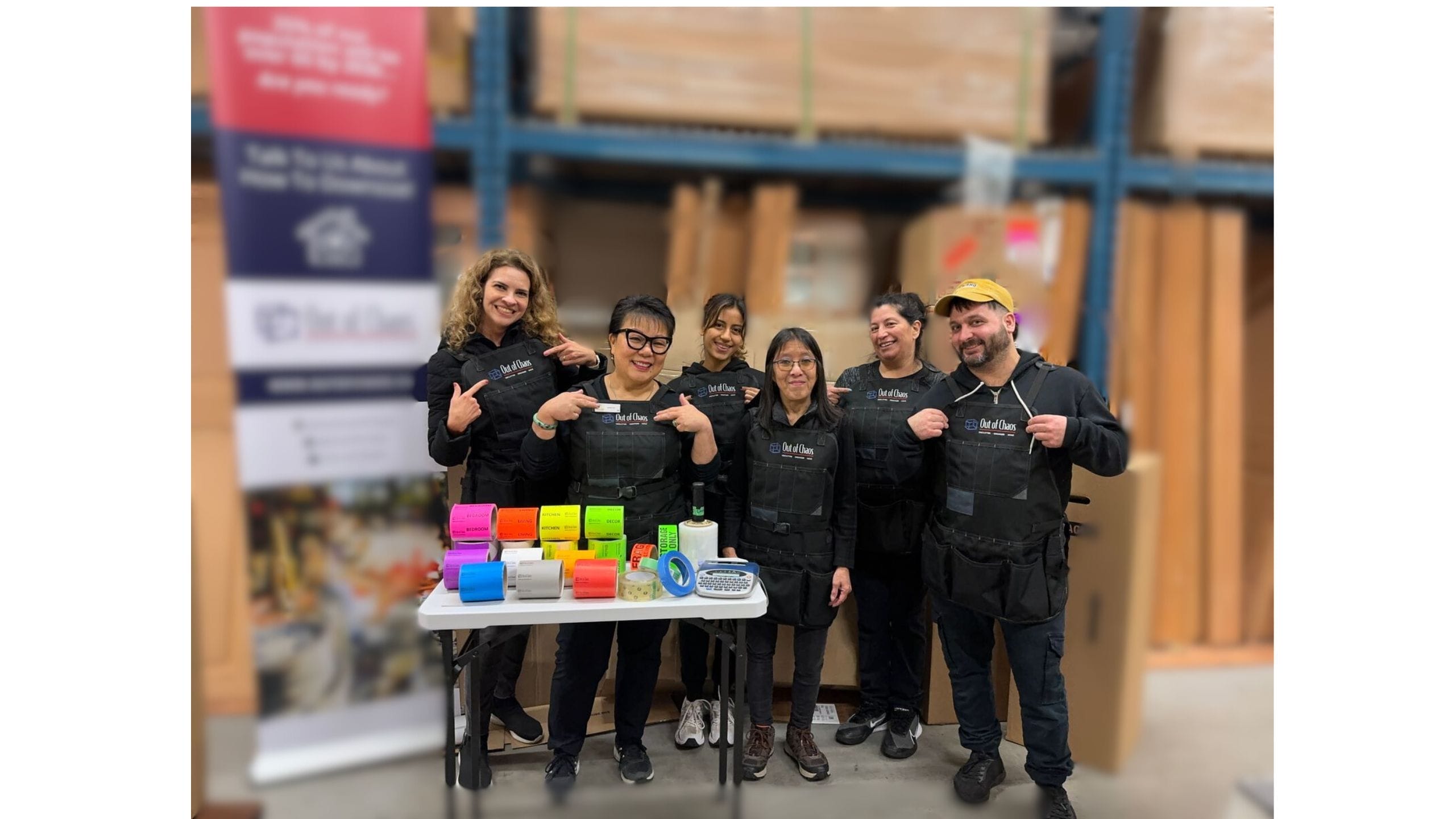 Group photo of Linda Chu's team, smiling and standing together while pointing at the "Out of Chaos" logo displayed on their work attire