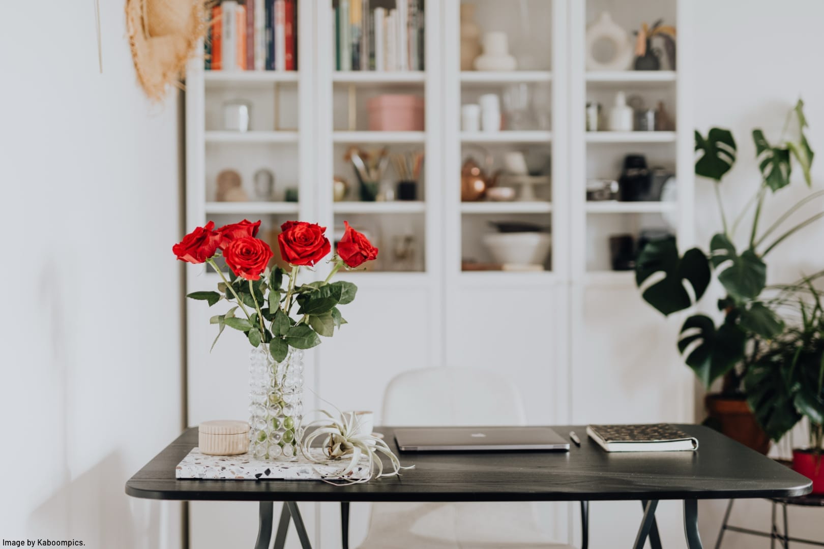 a bouquet of roses on a desk in front of white cabinets with glass doors containing decluttered and neatly organized books and home décor items